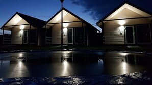 A row of three wooden cabins with attached porches, each with a porch light and a satellite dish. - Cozy Cottage in Family Holiday Resort, Jezierzany (Postomino)