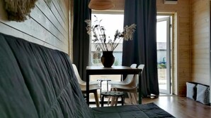 A cozy room with a wooden floor, a sofa, a table with chairs, and a window with dark curtains. - Cozy Cottage in Family Holiday Resort, Jezierzany (Postomino)