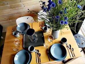 A wooden dining table set with blue plates, cutlery, and glasses, accompanied by a vase of blue flowers. - Cozy Cottage in Family Holiday Resort, Jezierzany (Postomino)