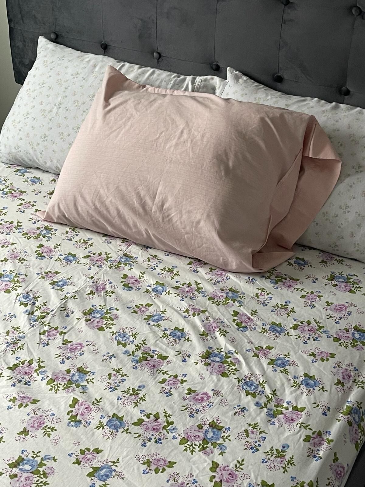 A bed with a floral-patterned bedspread and two pillows, one pink and one white with a subtle pattern.