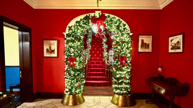 A staircase with a red carpet, flanked by two Christmas trees in gold pots, leading to a door with a red bow. - Summer Sale! Beakstown House Luxurious 5-bed Villa (Holycross)