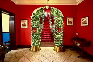Een trap met een rode loper, begrensd door twee kerstbomen in gouden potten, die leidt naar een deur met een rode strik.