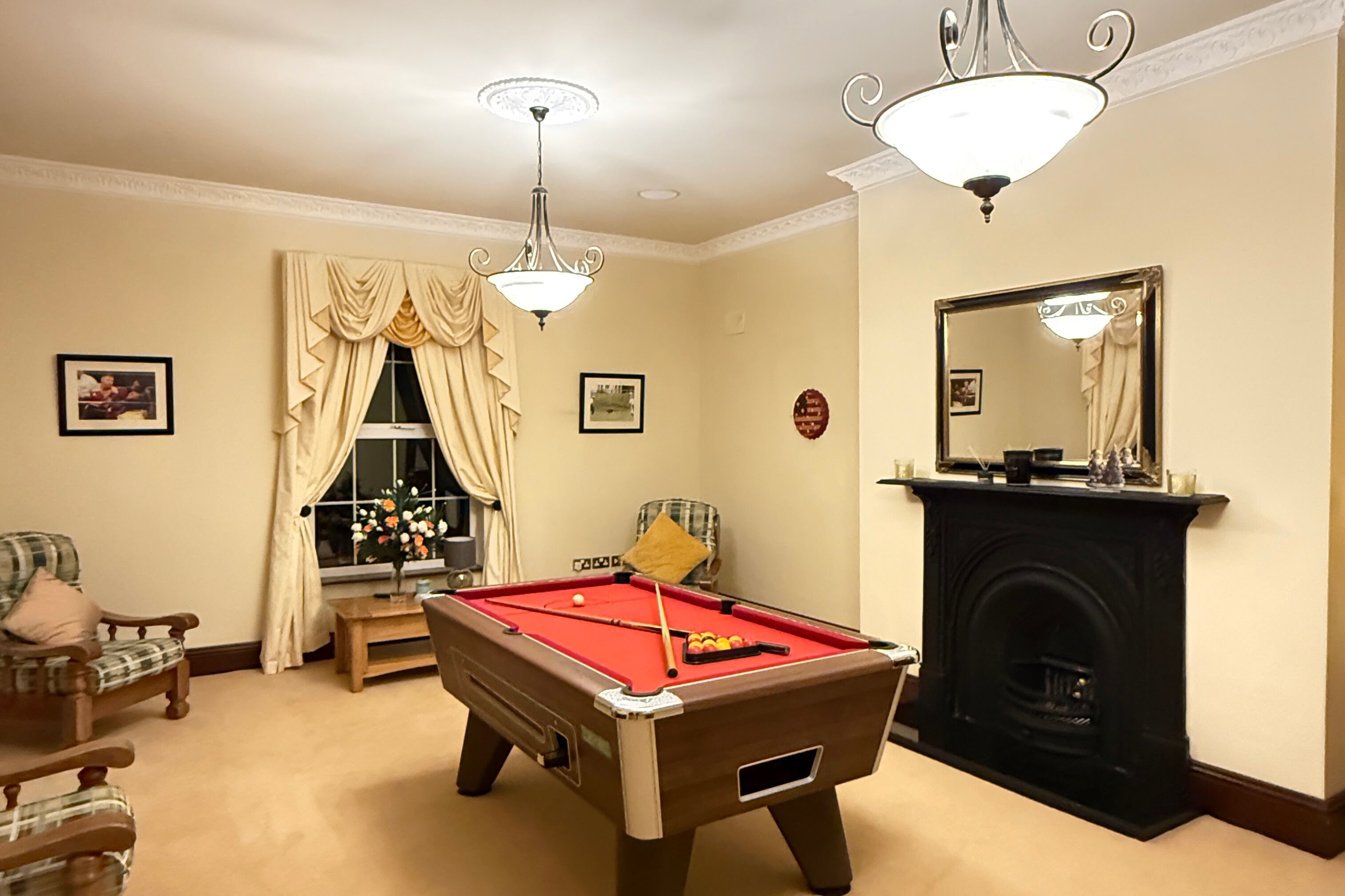A pool table in a room with a fireplace, a window with curtains, and a chandelier.
