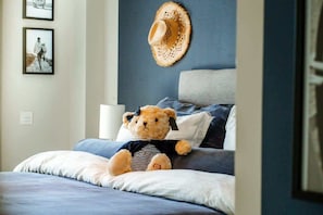 Una cama con un oso de peluche, un sombrero de paja en la pared y fotografías enmarcadas.