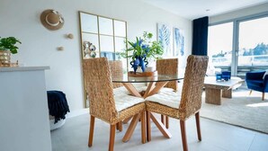 Ein Essbereich mit einem Glastisch, umgeben von Korbstühlen, einer Blumenvase und einem großen Fenster mit Aussicht.