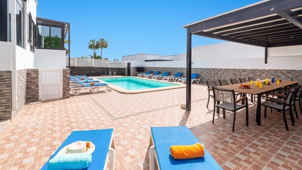 Uma área de piscina com espreguiçadeiras, uma mesa com bebidas e um espaço de estar coberto.