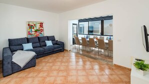 Sala de estar com um sofá cinza escuro, um cobertor branco e um quadro colorido na parede.