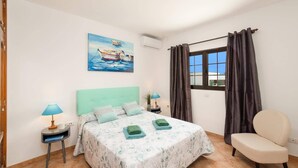 Quarto com cama, cadeira, quadro, janela e mesa de cabeceira.