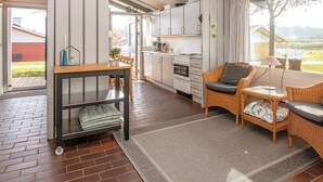 A modern kitchen with white cabinets, a dining area with a table and chairs, and a wicker sofa with cushions. - 6 Person Holiday Home in Aabenraa-by Traum (Aabenraa)