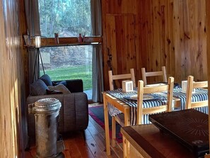 A cozy cabin interior with a sofa, wooden chairs, a small table, and a view of a forest through large windows. - Geum Red Bungalow, Antanhol, Coimbra (Coimbra)