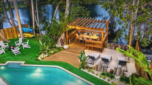 A backyard with a wooden deck, outdoor seating, a pool, and a view of a body of water. - Lakefront Lux Home • Pool_BBQ • Game Room & Kayak (Miami Springs)