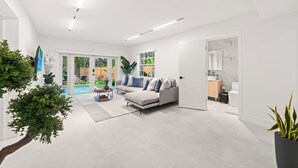 A modern living room with a grey sofa, a coffee table, and a large window overlooking a garden. - Lakefront Lux Home • Pool_BBQ • Game Room & Kayak (Miami Springs)