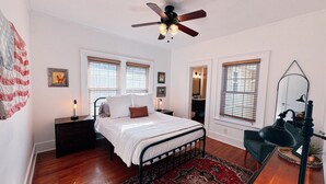 A bedroom with a bed, nightstands, a ceiling fan, and a large window with blinds.