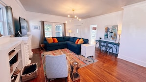 A living room with a sectional sofa, a fireplace, a dining area with a table and chairs, and a large window with curtains.