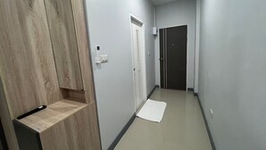 A narrow hallway with a wooden wardrobe, a white door with a vent, and a white mat on the floor. - Civilize apartment (Nonthaburi)