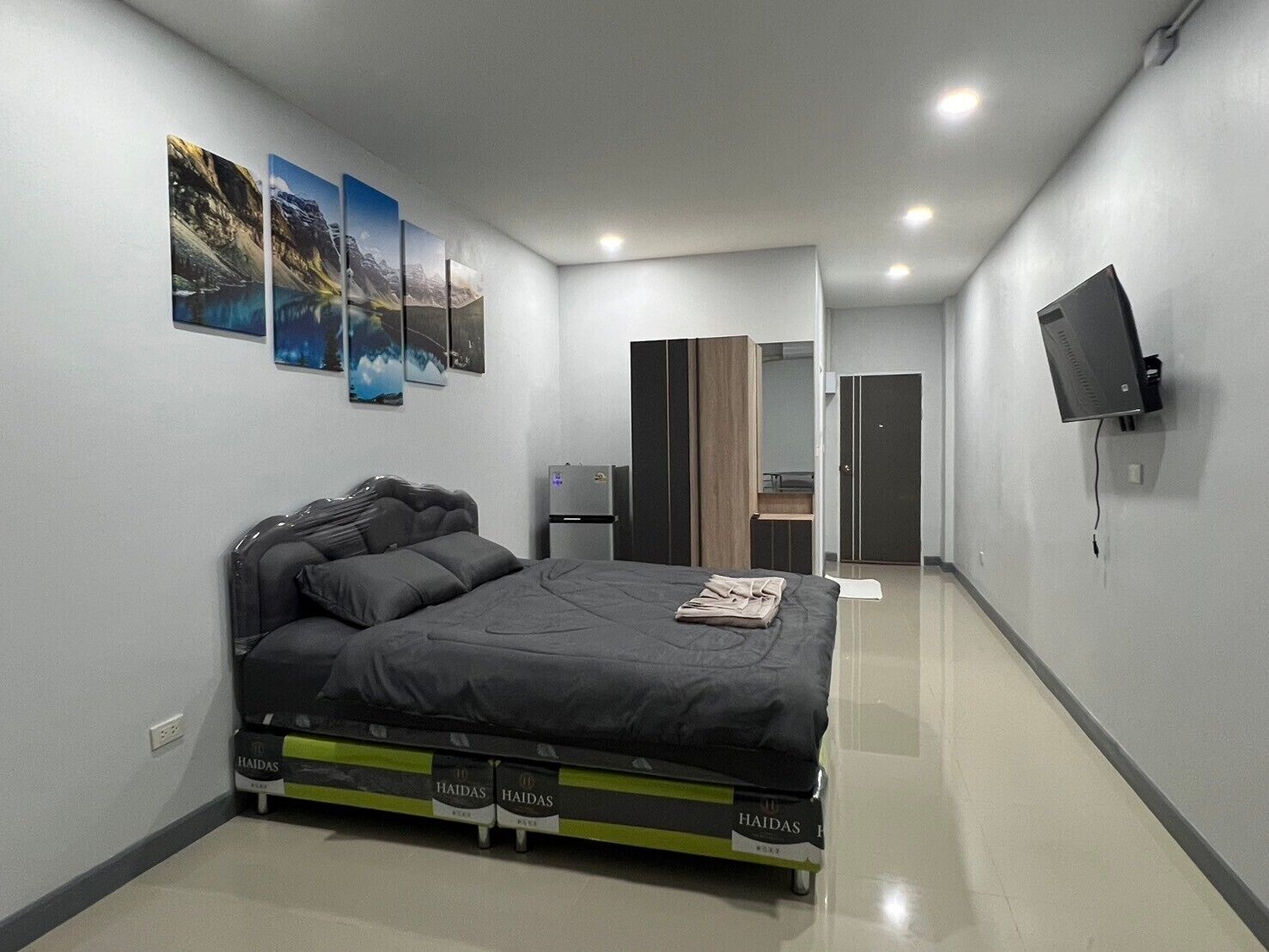 A modern bedroom with a bed, a flat-screen TV, and artwork on the wall.