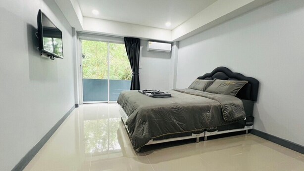 A modern bedroom with a bed, a flat-screen TV mounted on the wall, and a large window with curtains. - Civilize apartment (Nonthaburi)