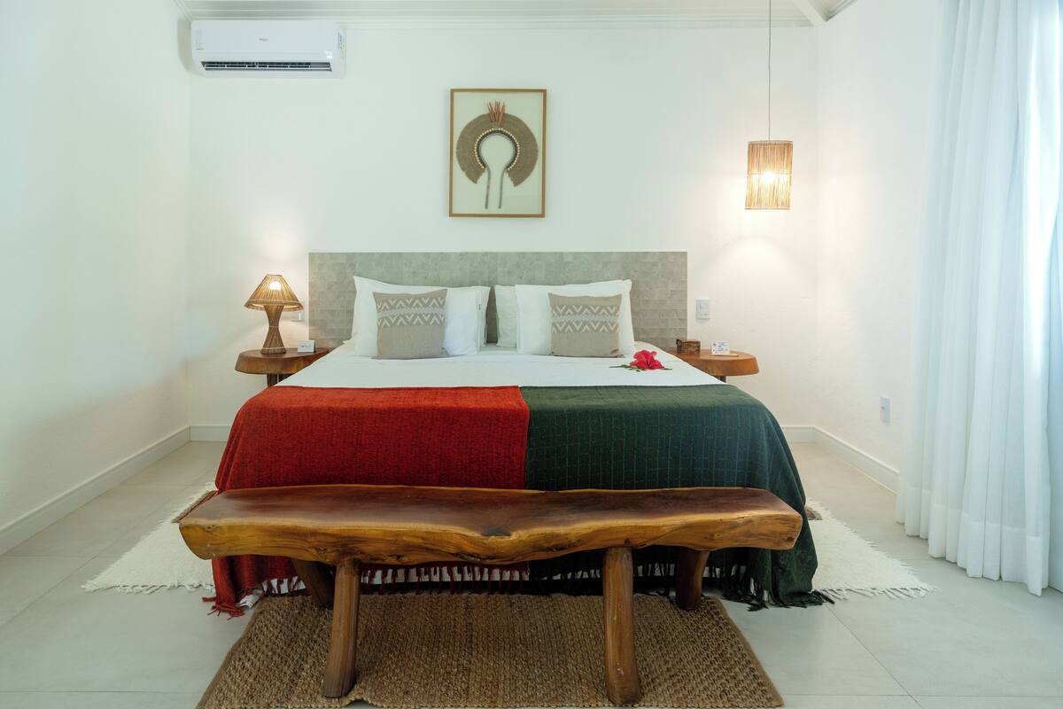A neatly arranged bedroom with a bed, bedside tables, a bench, and a wall-mounted air conditioner.