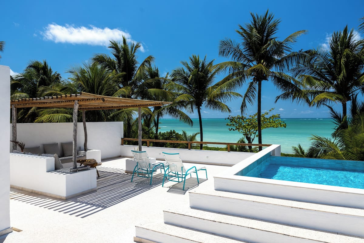 A rooftop pool area with a view of the ocean, surrounded by palm trees.