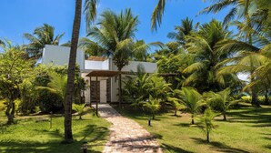 A pathway leading to a white building surrounded by palm trees and greenery. - Aldeia Beijupirá Pousada (Porto de Pedras)