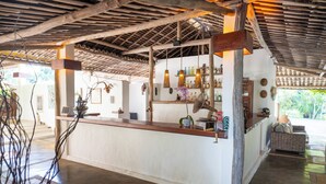 A bar area with a wooden ceiling, a counter with bottles, and a wicker sofa. - Aldeia Beijupirá Pousada (Porto de Pedras)