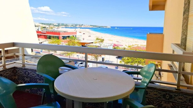 A balcony with a round table and green chairs, overlooking a beach with buildings in the background. - PRAIA DA ROCHA – ATLÂNTICO III (Portimão)