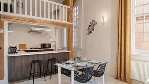 Une cuisine moderne avec des meubles blancs, un plan de travail en bois et un coin repas comprenant une table en verre et des chaises noires.