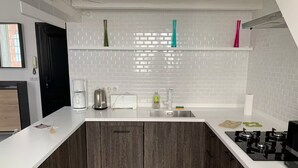 Une cuisine moderne avec un plan de travail blanc, des meubles de rangement en bois foncé, un évier en acier inoxydable et une cuisinière à gaz.