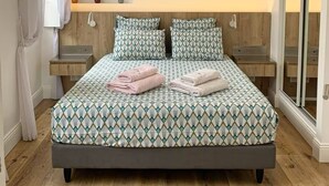 Une chambre à coucher avec un grand lit, deux tables de chevet, une commode, un luminaire suspendu et un miroir.