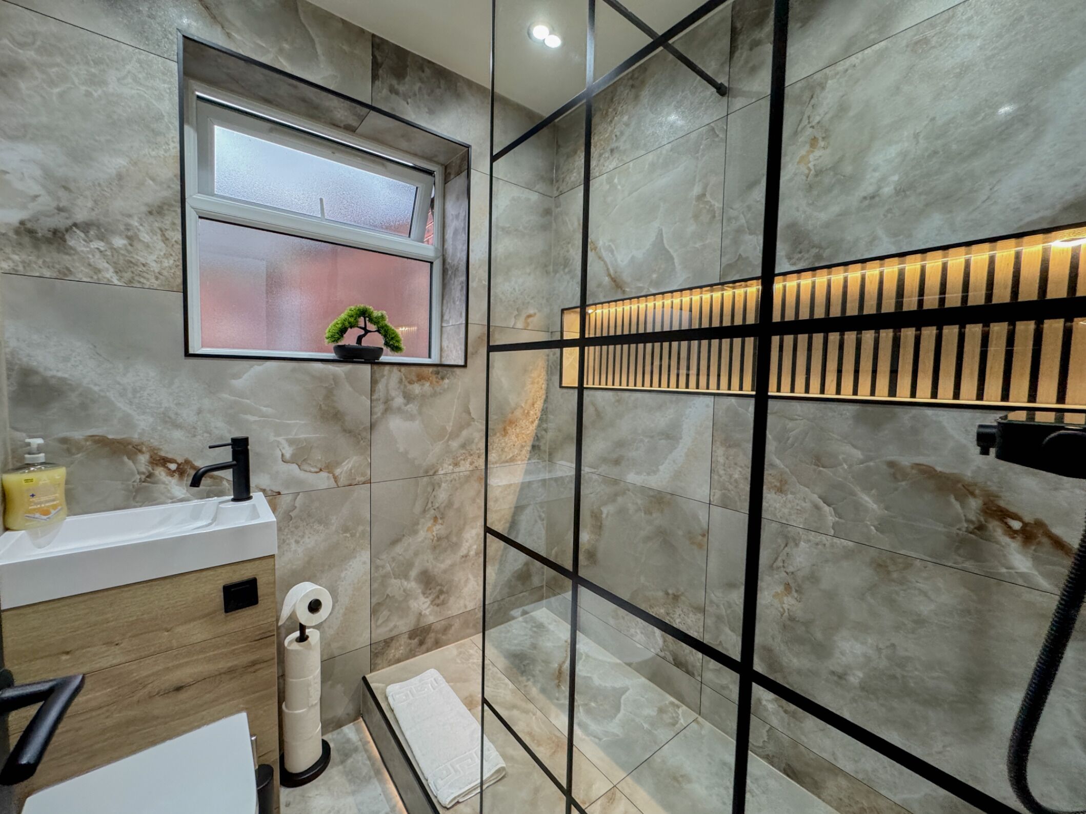 Un bagno moderno con una parete in marmo, una piccola finestra con una pianta, un appendi-asciugamani e un portasciugamani.