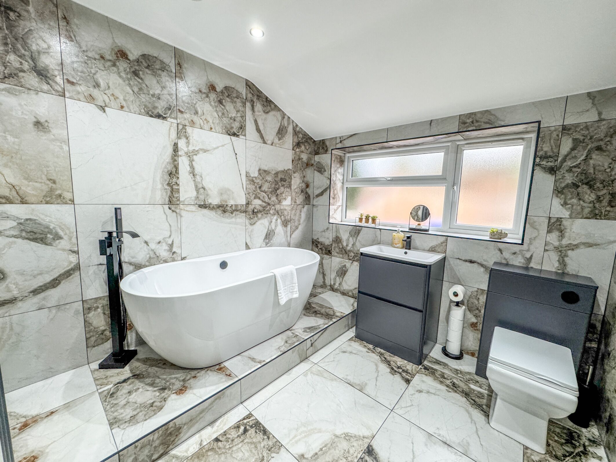 A modern bathroom with a freestanding bathtub, a vanity with a mirror, and a toilet.