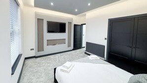 A modern bedroom with a bed, a TV mounted on the wall, a radiator, and a large wardrobe. - Miles House (Boston)