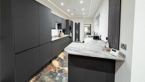 A modern kitchen with dark cabinetry, a marble countertop, and a unique patterned floor. - Miles House (Boston)