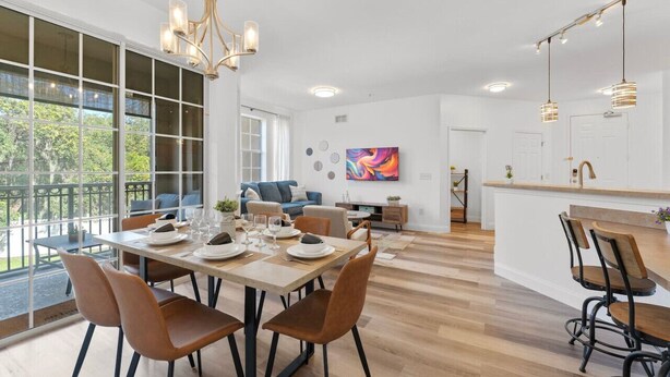 A modern kitchen with a dining area, large windows, and a view of greenery.