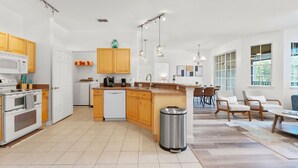 A modern kitchen with wooden cabinets, a central island, and a dining area with chairs.