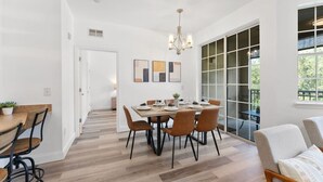 A dining area with a wooden table and chairs, a chandelier, and a view through a glass door to an outdoor area.
