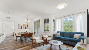 A modern living room with a blue sofa, wooden chairs, a dining table, and a coffee table.