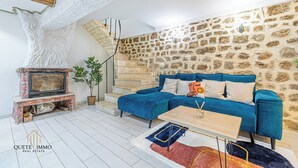 A living room with a stone wall, a blue sofa, a fireplace, and a staircase. - Renovated House: Peace & Comfort 20 min from Monaco (Peille)