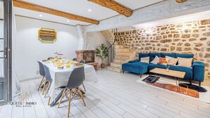 A dining area with a table set for breakfast, a blue sofa, and a stone wall. - Renovated House: Peace & Comfort 20 min from Monaco (Peille)