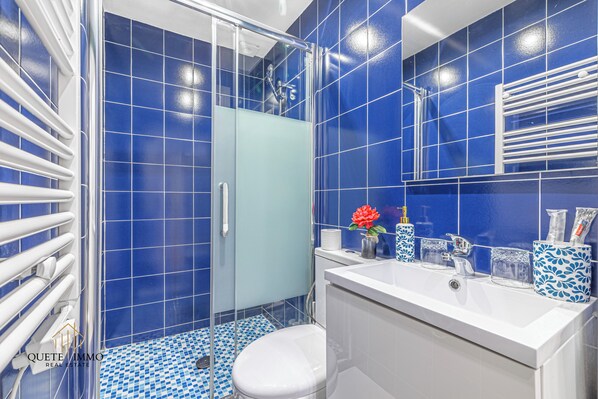 Een badkamer met blauwe tegels, een witte wastafel en een douchecabine van glas.