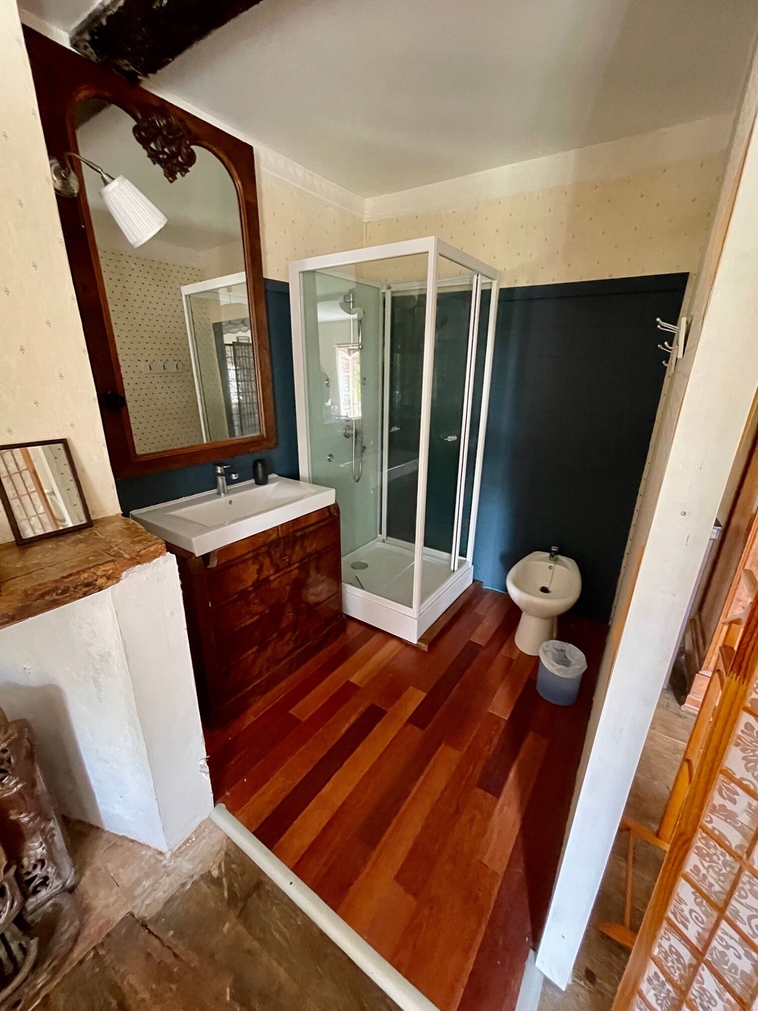 A bathroom with a wooden floor, a white sink, a glass-enclosed shower, and a toilet.