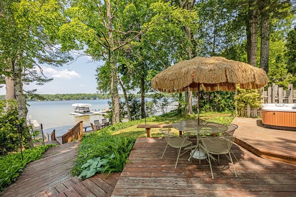 Une terrasse en bois avec une table et des chaises, un jacuzzi et un parasol en chaume.