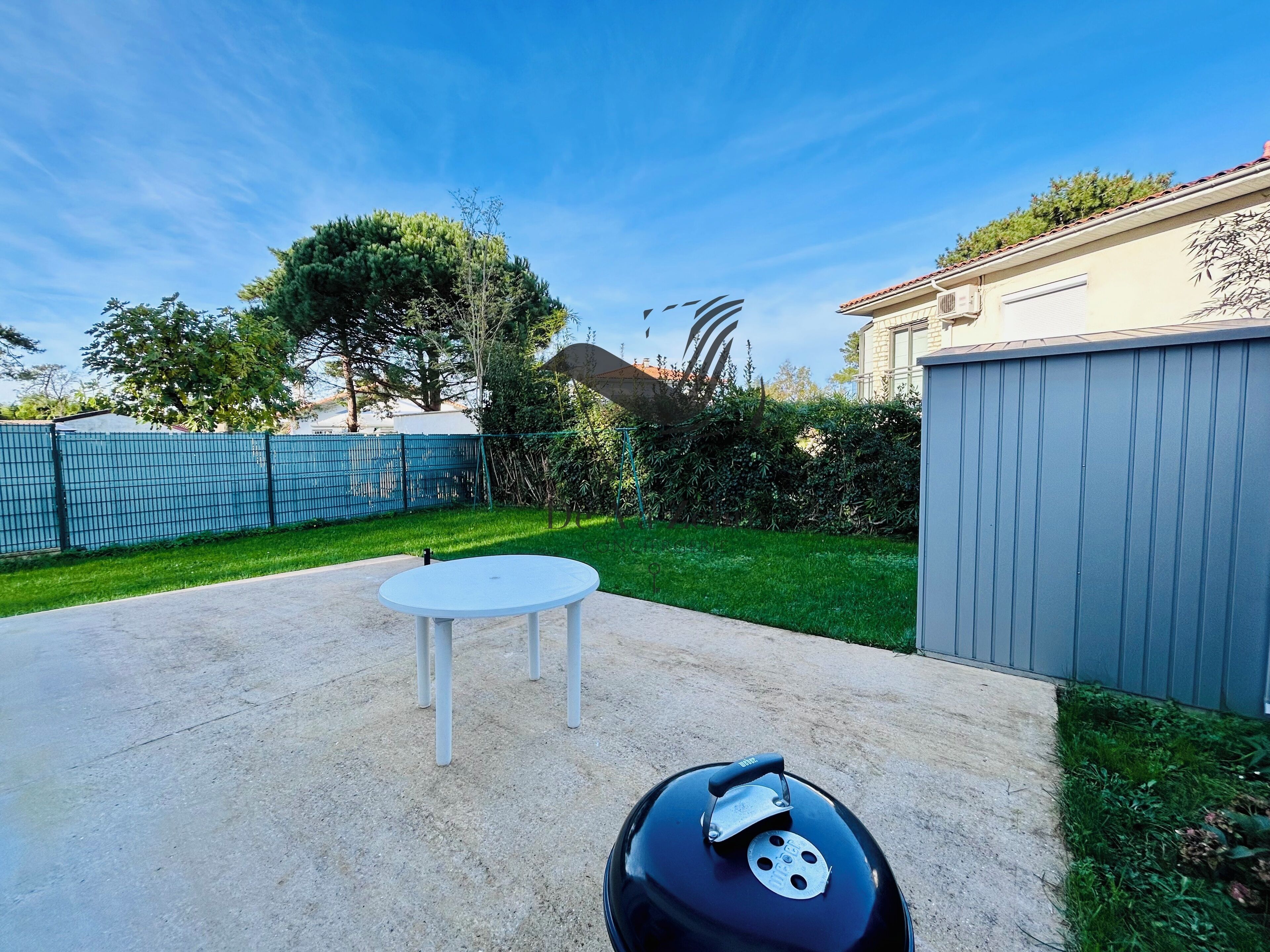 Un jardin avec un barbecue, une table ronde et une clôture bleue.