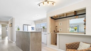 A modern kitchen with a central island, a dining area with a patterned sofa, and a view of the outdoors through a window.