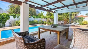 A covered outdoor area with a pool, wicker furniture, and a table.