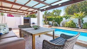 An outdoor patio with a pool, wicker furniture, and a covered area with a metal roof.