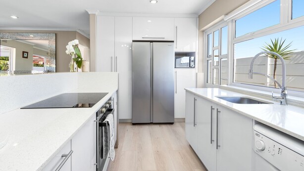 A modern kitchen with white cabinetry, a stainless steel refrigerator, a built-in oven, and a window with a view of the outside.
