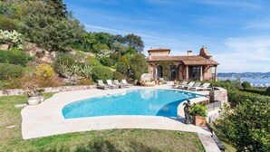 Ein privater Pool mit Liegestühlen, ein Steinhaus und Blick aufs Meer.