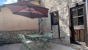A stone building with a patio area featuring a table and chairs, a large umbrella, and a stone wall.