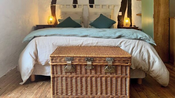 A bed with a headboard, two bedside lamps, and a wicker chest in front.